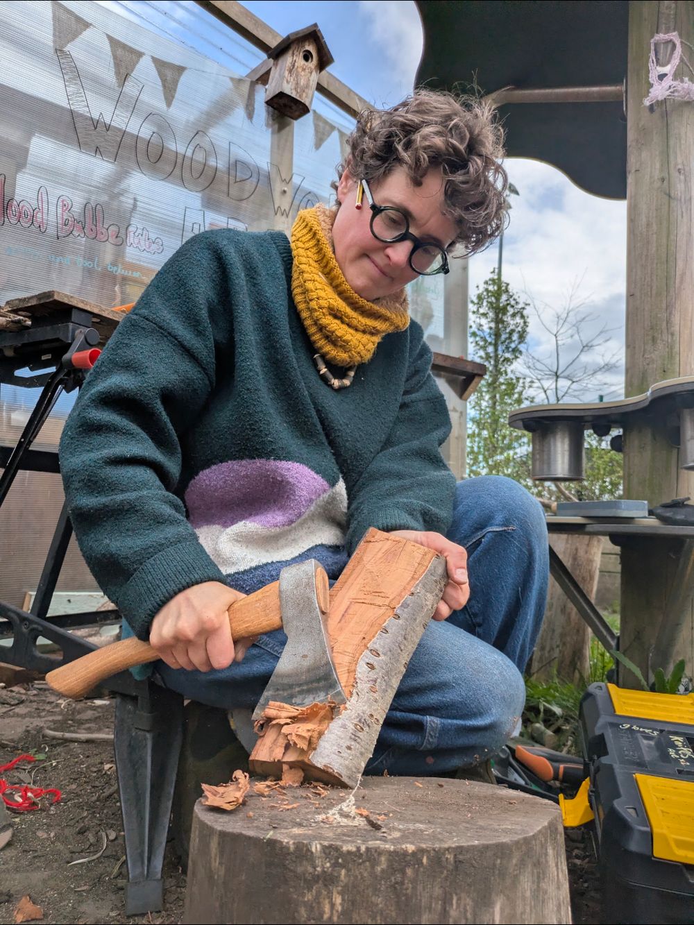 Holly shaping a log with an axe on a chopping block