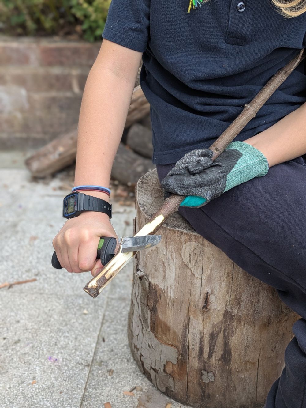 A child in school uniform carving a stick with a knife