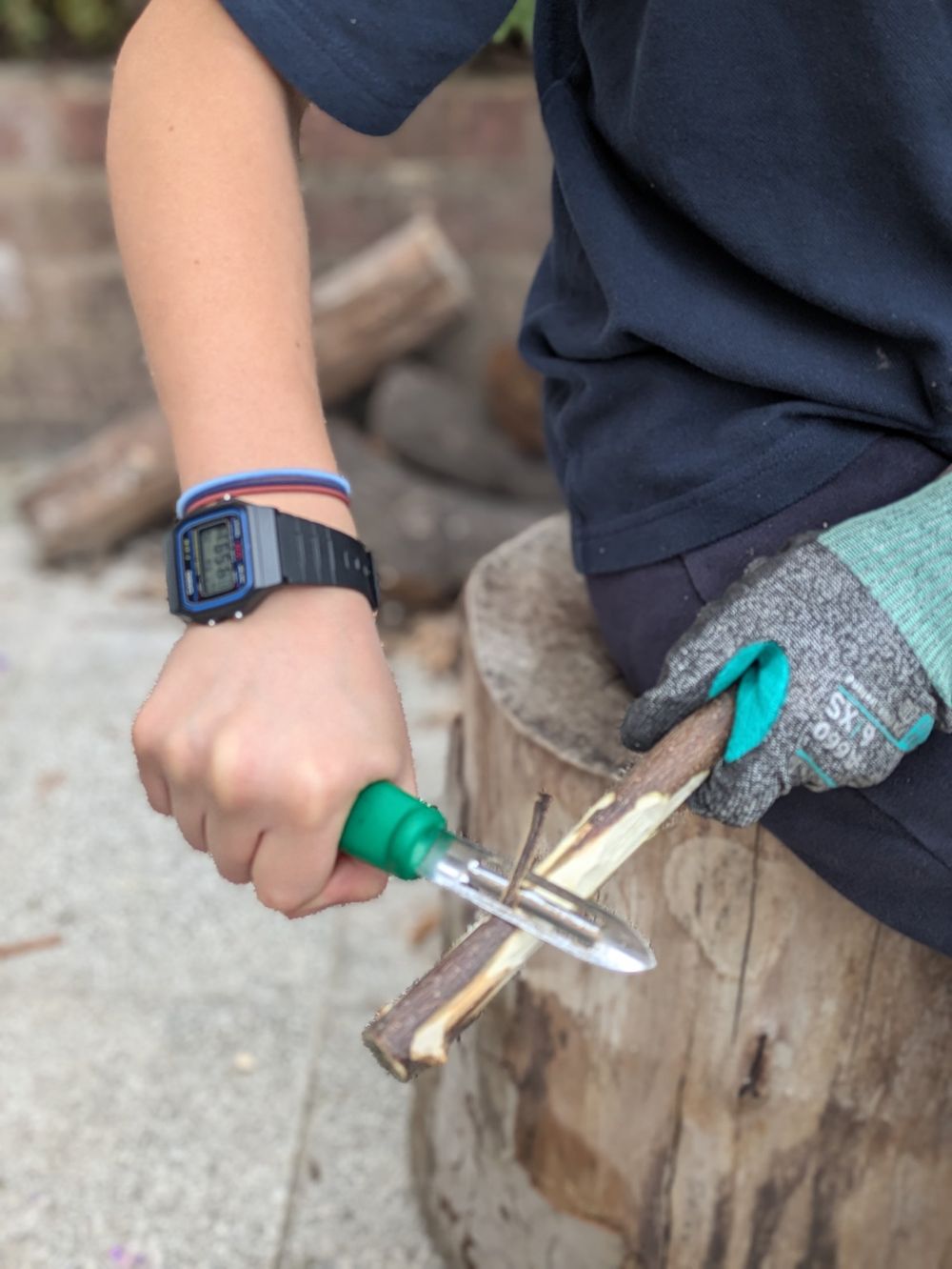A child in school uniform whittling a stick with a peeler, wearing a safety glove