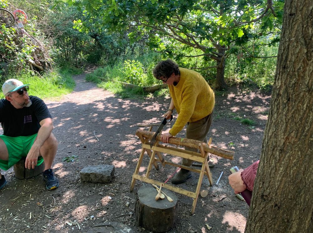 Holly sawing a log in the park while two adults watch